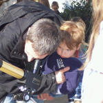 Toddler and father bending over a solar telescope
